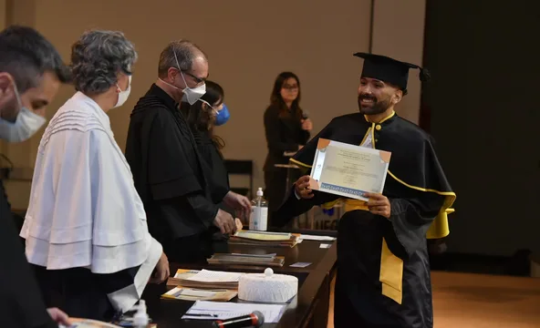 Elias de beca recebendo o diploma no palco da formatura.