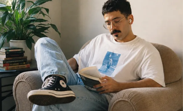 Elias em pé, encostado numa parede, olhando para a câmera.
